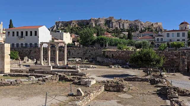 Athens, Greece - 22 June 2026. View from Hadrian's Library featuring the four-column fa&ccedil;ade, excavated foundations, the Acropolis hill, the Parthenon, and nearby Plaka buildings.