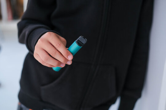 A teenager is holding a violet vape. A dangerous addiction. Vaping among teenagers.