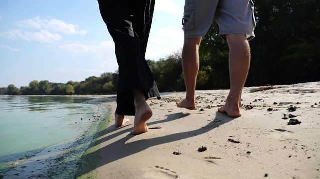 Bare feet of couple stepping together along sand beach at coastline. Male and female legs of pair walking near seaside. Happy lovers going along sandy shore. Concept of summer vacation or holiday