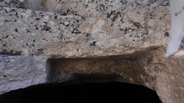 Salina, Malta - a young boy stands before a dark, rectangular entrance carved into weathered limestone rock, marking one of the ancient Paleo-Christian catacombs surrounded by layered stone blocks.