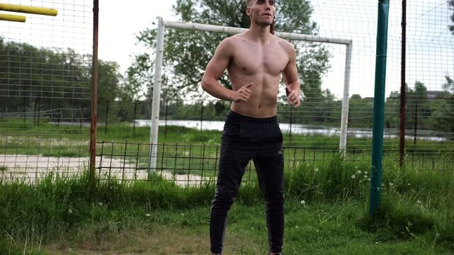 Male shirtless athlete doing squats at sports ground. Young sportsman working at summer nature. Strong sporty man exercising outdoor. Concept of active and sportive lifestyle. Slow motion
