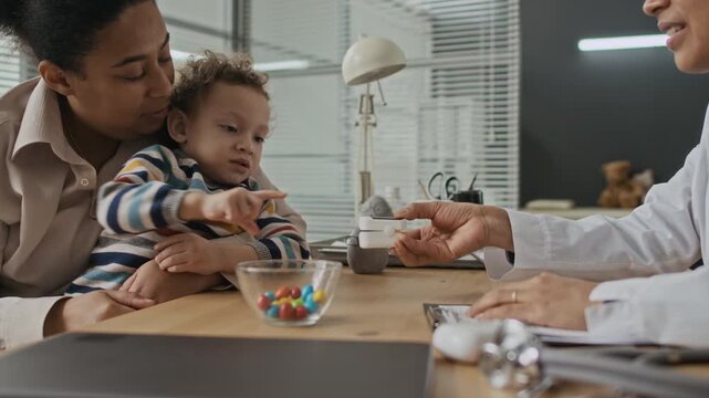 Biracial mother holding young child during medical checkup with pediatrician using pulse oximeter. Perfect for pediatric clinic promotions and family healthcare marketing videos