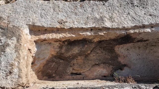 Salina, Malta - weathered limestone blocks bearing small carved openings and lichen growth surround the ancient Paleo-Christian catacomb complex, with wild plants sprouting between the ancient stonewo