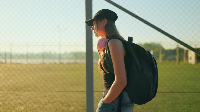 Inspired youngster walking beside metal fence under bright sun.