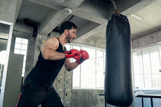 Boxer striking a heavy bag in a gym, promoting strength, endurance, boxing and fitness training.