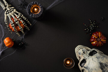 Obraz premium Happy Halloween spooky flat lay with skull, skeleton hand holding pumpkin, candles and spiders