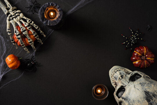 Happy Halloween spooky flat lay with skull, skeleton hand holding pumpkin, candles and spiders