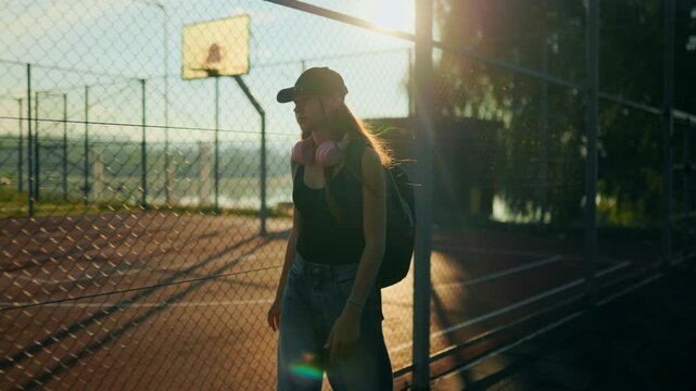 Inspired preteen walking past metal barrier under bright sun glare.