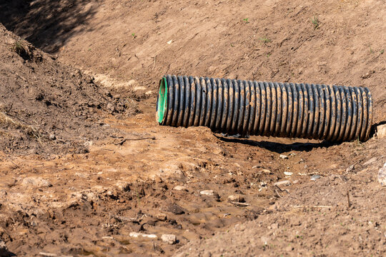 Close view of a robust ribbed culvert pipe placed inside a dug-out earthen channel, showcasing rural infrastructure development and soil preparation.