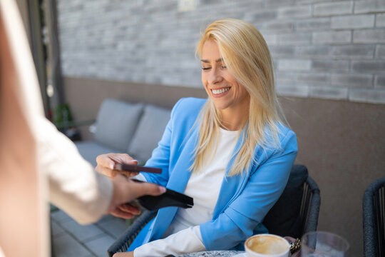 Woman making contactless payment using smartphone at cafe
