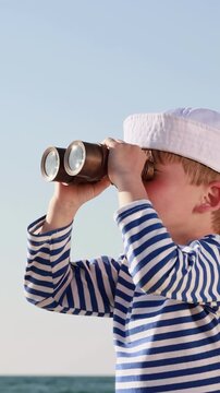A happy child is playing on a sandy beach. Funny boy pretends to be a sailor during summer vacation. A kid against a background of blue summer sky and sea. Vertical slowmo video