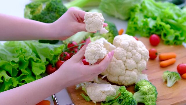 female hands cut cauliflower with a knife on a cutting kitchen table and put the pieces in glass transparent bowl The chef cuts cauliflower for cooking. Healthy and wholesome natural food