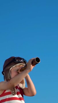 A happy child is playing on a sandy beach. Funny boy pretends to be a sailor during summer vacation. A kid against a background of blue summer sky and sea. Vertical slowmo video