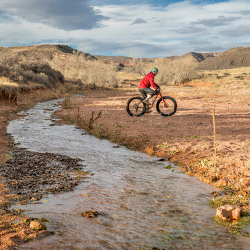 a male riding a fat bike across a stream in Red Mountain Open Space, Colorado , late fall scenery