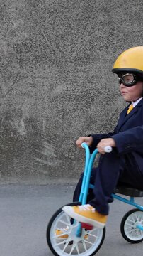 A happy child pretends to be a businessman. Funny kid rides a bike outdoors. A boy has fun during the summer holidays. Back to school, the concept of a business idea. Slow motion, vertical video