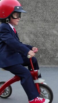 A happy child pretends to be a businessman. Funny kid rides a bike outdoors. A boy has fun during the summer holidays. Back to school, the concept of a business idea. Slow motion, vertical video