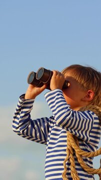 A happy child is playing on a sandy beach. Funny boy pretends to be a sailor during summer vacation. A kid against a background of blue summer sky and sea. Vertical slowmo video