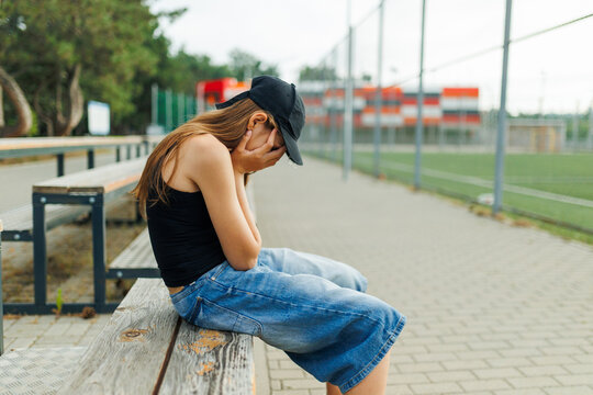 Sad teenage girl sitting on a bench covering her face with hands.