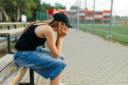 Unhappy teenage girl sitting alone on a bench covering her face.