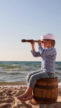 A happy child is playing on a sandy beach. Funny boy pretends to be a sailor during summer vacation. A kid against a background of blue summer sky and sea. Vertical video