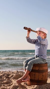 A happy child is playing on a sandy beach. Funny boy pretends to be a sailor during summer vacation. A kid against a background of blue summer sky and sea. Vertical video