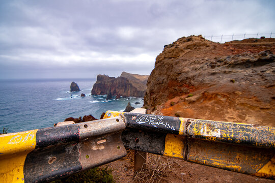 Old weathered yellow guardrail with scratches overlooking rugged volcanic cliffs and ocean in Madeira