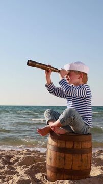 A happy child is playing on a sandy beach. Funny boy pretends to be a sailor during summer vacation. A kid against a background of blue summer sky and sea. Vertical video