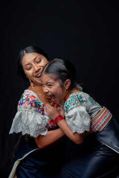 Indigenous Kichwa mother and daughter from Otavalo, Ecuador, wearing traditional hand-embroidered blouses and anaco sharing affectionate moments of cultural heritage in a studio portrait