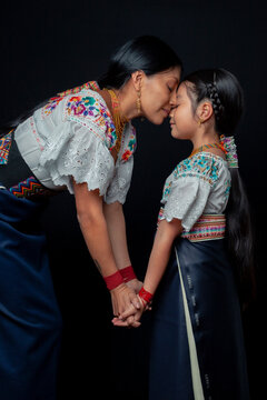 Indigenous Kichwa mother and daughter from Otavalo, Ecuador, wearing traditional hand-embroidered blouses and anaco sharing affectionate moments of cultural heritage in a studio portrait