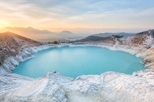 Calm volcanic crater lake with milky blue water and white deposits.