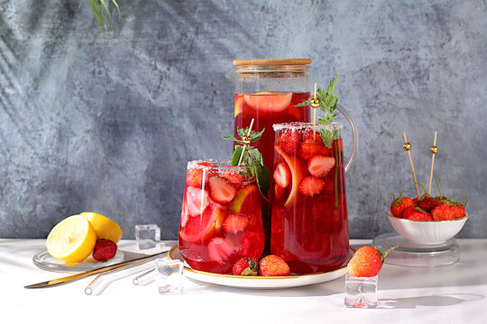 Strawberry Iced Tea or Mint Lemon Cocktail is a refreshing summer drink recipe. Glasses with berry fruit lemonade on a light concrete table, detox diet and weight loss concept, restaurant menu.