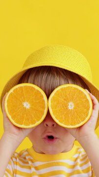 A happy child holds orange slices in his hands like sunglasses. Slow motion, vertical video