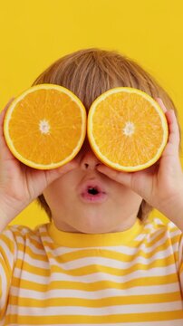A happy child holds orange slices in his hands like sunglasses. Slow motion, vertical video