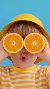 A happy child holds orange slices in his hands like sunglasses. Slow motion, vertical video