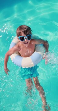 A happy child is having fun on the summer vacation. A kid is swimming in the pool. Vertical video. Slow motion