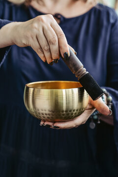 Woman playing a Tibetan singing bowl with a wooden mallet during a sound healing meditation session.