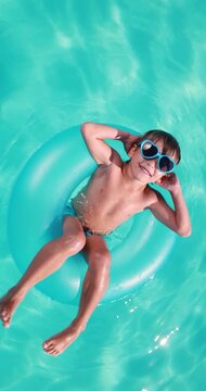 A happy child is having fun on the summer vacation. A kid is swimming in the pool. Vertical video. Slow motion