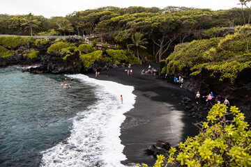 Visitors walking along the black sand beach at Waianapanapa State Park, Maui © Zach