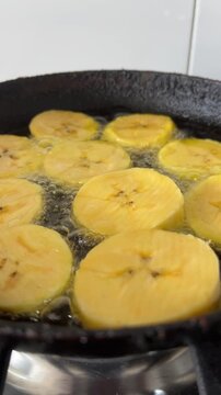 Plantain slices frying in hot oil on cast iron pan