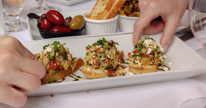 Hands reaching for bruschetta appetizers at restaurant table