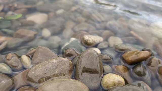 Gentle river water flowing over smooth colorful stones