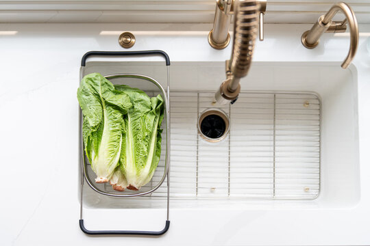 Unwashed romaine lettuce in colander at kitchen sink overhead