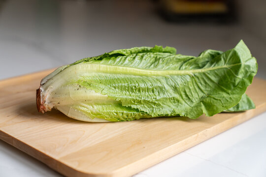 Whole unwashed romaine lettuce head with visible root on cutting board