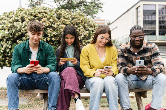 Happy friends using cell phones and social media app - Students sitting in university campus having fun on the smartphones