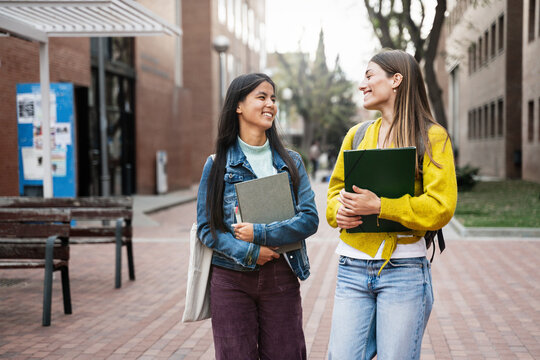 Diverse international student girl friends walking and talking at university Campus after classes 