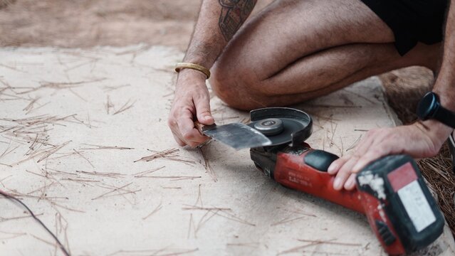 Worker sharpening a metal blade with an angle grinder outdoors