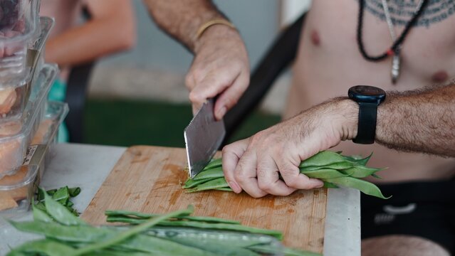 Man dicing fresh green beans on a board, prepping paella ingredients