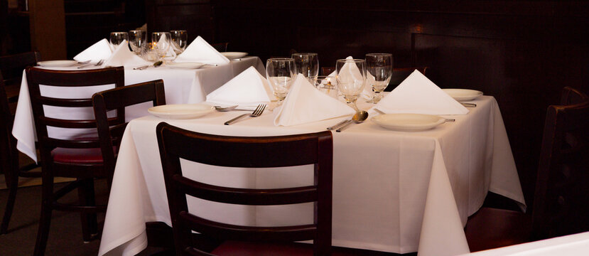 Empty restaurant tables with white tablecloths and folded napkins