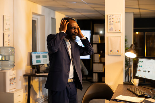 Black man dancing in the office at night with wireless headphones, expressing groovy moves and energetic rhythm after hours. Cheerful employee enjoying music playlist during overtime.