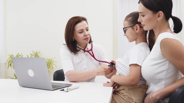 Pediatrician listening to a little girl's breathing with a stethoscope while her mother watches during a medical examination. Concept pediatric care, child healthcare, family medicine, preventive medi
